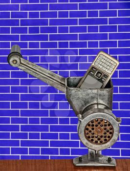 Old mobile phone in meat grinder on blue brick wall background taken closeup.