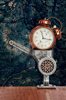Bronze vintage alarm clock in meat grinder on blue grunge wall background.