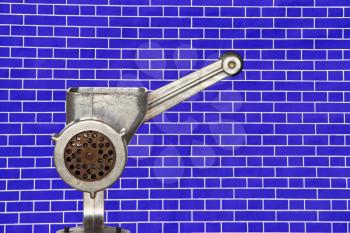 Metal meat grinder on blue brick wall background taken closeup.
