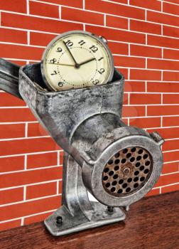 Alarm clock in meat grinder on red brick wall background taken closeup.
