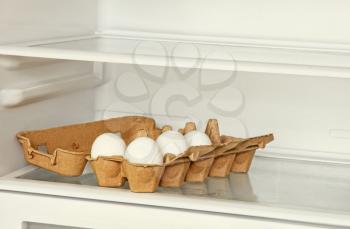Fresh eggs in a paper box on refrigerator shelf.