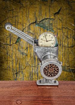 Alarm clock in meat grinder on grunge scratched background.Toned image.