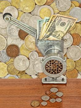 Dollar banknotes in meat grinder and coins on table on lot of different coins background.Money and busines concept.