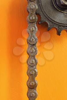 Black metal cogwheel and chain on orange background taken closeup.