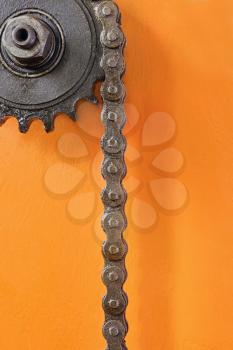 Metal cogwheel with chain on orange background taken closeup.