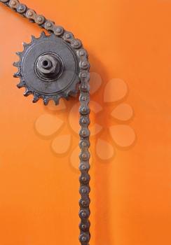 Metal cogwheel and black chain on orange background taken closeup.