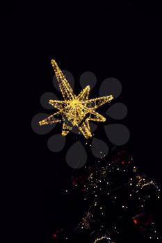 Golden Bethlehem star topped on christmas tree in darkness.