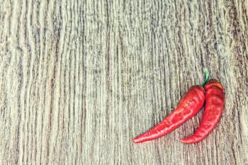 Two Red Hot Chili peppers on grunge wooden background taken closeup.Toned image.