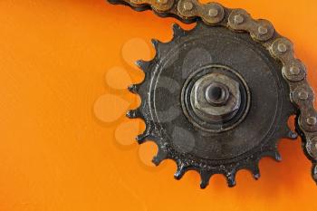 Metal cogwheel and chain taken closeup on orange background.