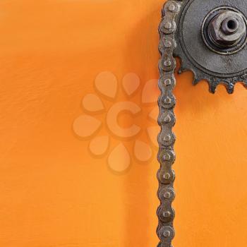 Metal cogwheel and black chain on orange background with empty space for text.