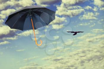 Black umbrella flies in dramatic sky against of white clouds.Mary Poppins Umbrella.Wind of change concept.