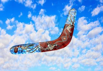 Multicolored australian boomerang flies in sky against of pure white clouds.