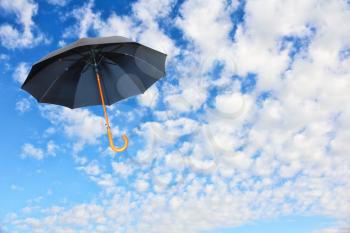 Wind of change concept.Black umbrella flies in sky against of pure white clouds.Mary Poppins Umbrella.