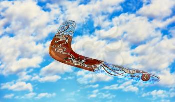 Multicolored australian boomerang in flight against of blue sky and pure white clouds.
