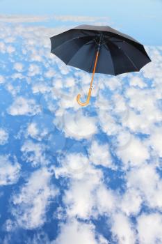 Black umbrella flies in sky against of white clouds.Mary Poppins Umbrella.Wind of change concept.