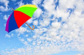 Wind of change concept.Multicolored umbrella flies in sky against of pure white clouds.Mary Poppins Umbrella.