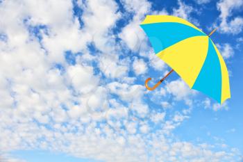 Umbrella in Ukrainian flag colors flies in sky against of pure white clouds.Mary Poppins Umbrella.Wind of change concept.