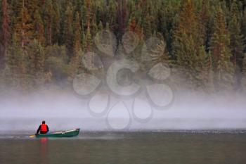 Man in canoe near morning mist on lake