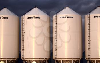 Four sunlit silos with storm clouds behind
