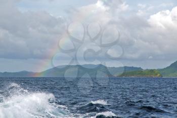 from a boat the rainbow from  ocean and island in background