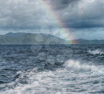 from a boat the rainbow from  ocean and island in background