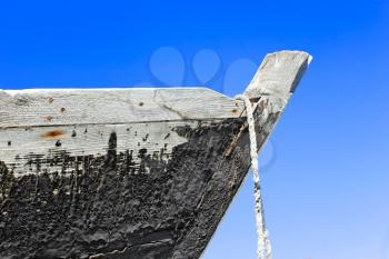 The prow of the old wooden boat with a tarred surface against blue sky