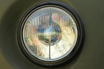 Old car round headlight against a dark green painted rusty body