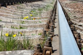 Railway rail in spring season close-up. Dandelions flowering between railroad ties among gravel