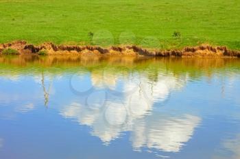 Blue sky with white clouds reflected on a ponds water surface in springtime