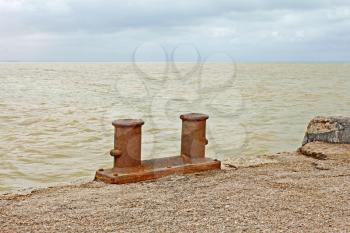 Steel rusty dual berth bitt on a fragment of old concrete pier on the background yellowish sandy seawater after the st