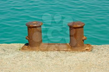 Steel rusty dual mooring bitt on a fragment of old concrete pier on the background turquoise sea water in calm