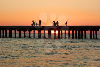 Groups of people on the old pier admire the beautiful sunset over the Black Sea coast in Crimea, Ukraine