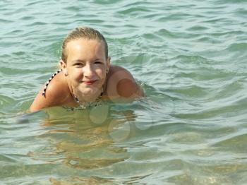 Smiling teenage girl swimming in sea water in warm sunny weather