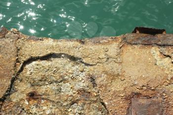 Detail of old reinforced concrete pier over the water in a bright sunlight
