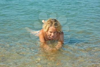 Teenage girl lies in the shallow coastal sea water with pebbly bottom in warm sunny weather