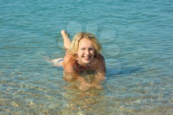 Beautiful smiling teenage girl lying in the shallow coastal sea water with pebbly bottom in sunny weather