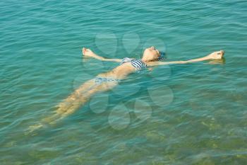 Teen girl lying on the turquoise sea water surface in shallow coastal area