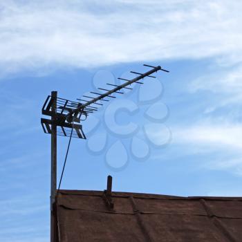 Television antenna over old metal roof on the sky background