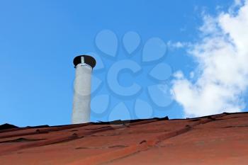 Chimney pipe over the old tinny roof against the blue sky