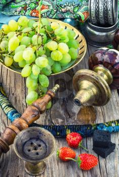 details vintage smoking hookah on wooden table on background of ripe grapes and strawberries