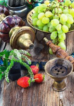 Old smoking  hookah and bunch of grapes on wooden surface.