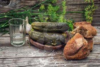 Pickled cucumbers with dill and a glass on wooden background in country style.Photo tinted.