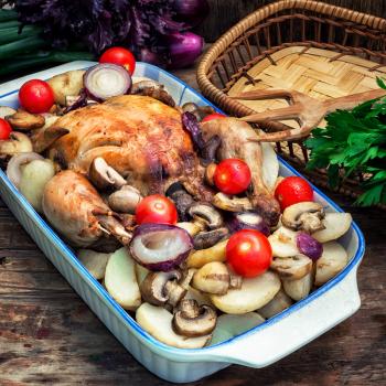 young chicken baked with potatoes,mushrooms and vegetables in the baking dish.
