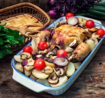 young chicken baked with potatoes,mushrooms and vegetables in the baking dish.