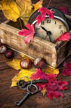 covered with autumn leaves old alarm clock in wooden box on the table