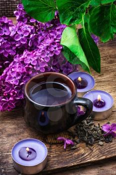 fragrant spring flower tea on the background of burning candles and lilac bouquet