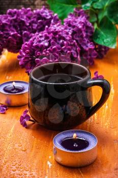 fragrant spring flower tea on the background of burning candles and lilac bouquet