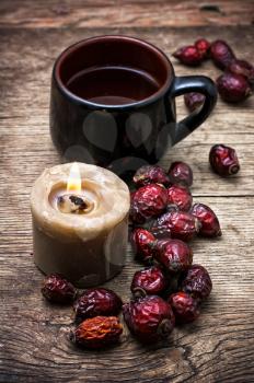 mug of tea and dried berries of the wild rose on wooden table in rustic style