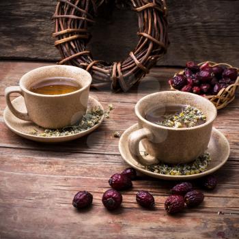 Two ceramic cups brewed tea with rosehip and chamomile amid bundles of licorice root