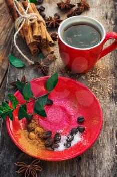 Red glass Cup with coffee on wooden background strewn with aromatic spices to drink